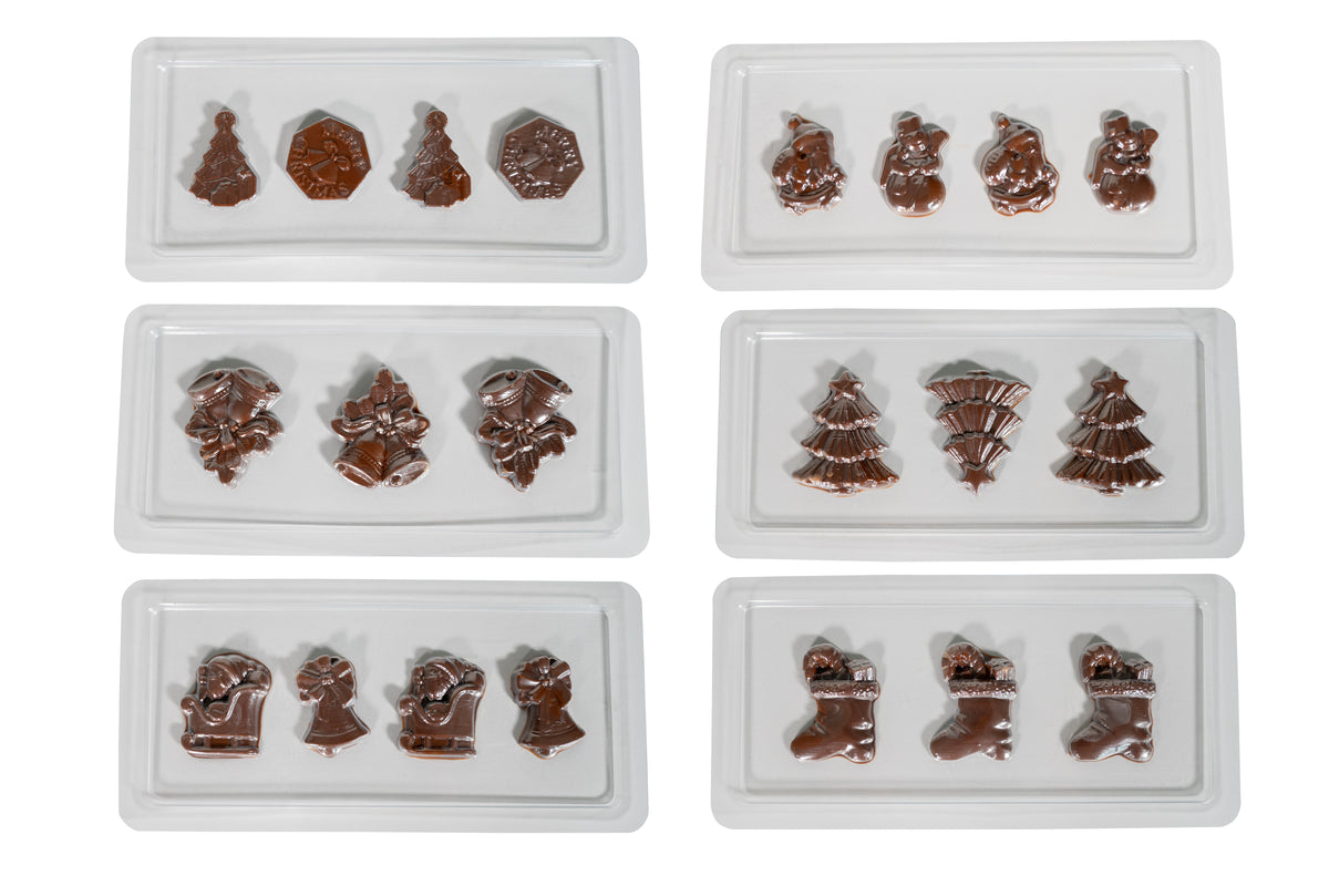 Sechs weiße Tabletts aus der Chocolatier Weihnachtsedition von Unold zeigen glänzende Schokoladenstücke in Form von Weihnachtsbäumen, Strümpfen, Glocken, Schneemännern und anderen festlichen Weihnachtsmotiven auf weißem Hintergrund.