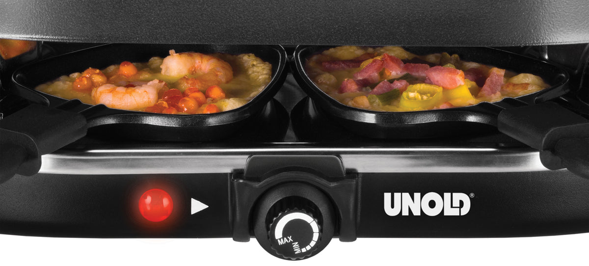 Nahaufnahme des Unold Raclette Gourmet Grills mit zwei kleinen Pfännchen, in denen Garnelen, Gemüse und Speck gegart werden. Auf der Vorderseite sind die rote Kontrollleuchte und ein Temperaturregler zu sehen.