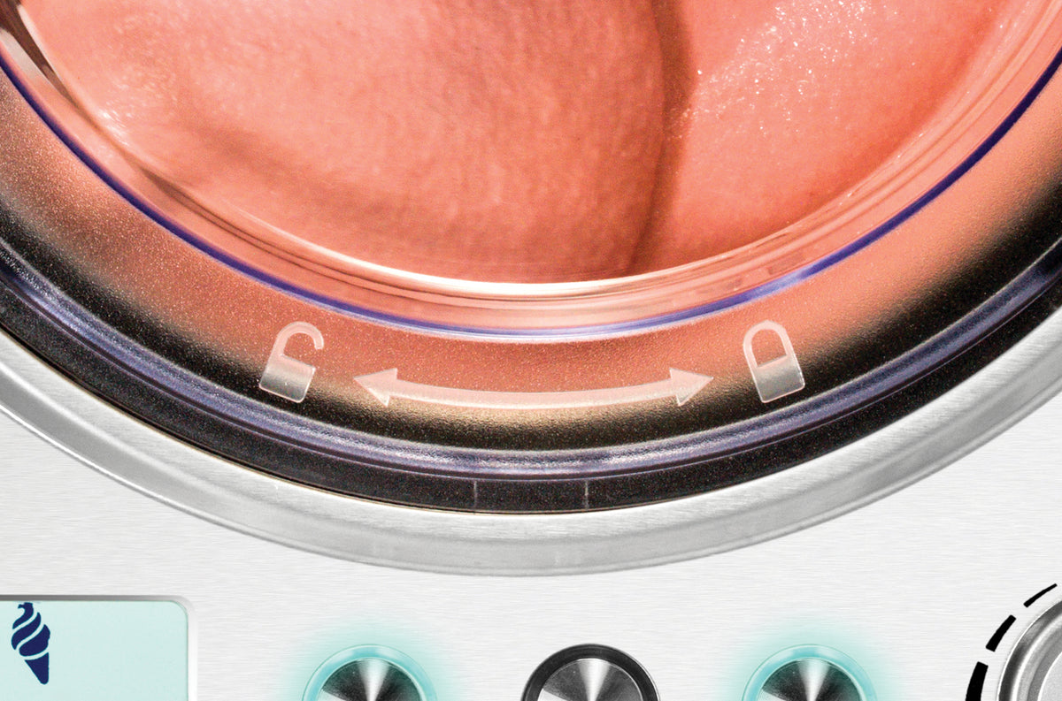 Eine Nahaufnahme der Tür der Unold Eismaschine Exklusiv 2 L mit einer gegen das Glas gedrückten Zunge und darunter angezeigten Verriegelungs-/Entriegelungssymbolen.