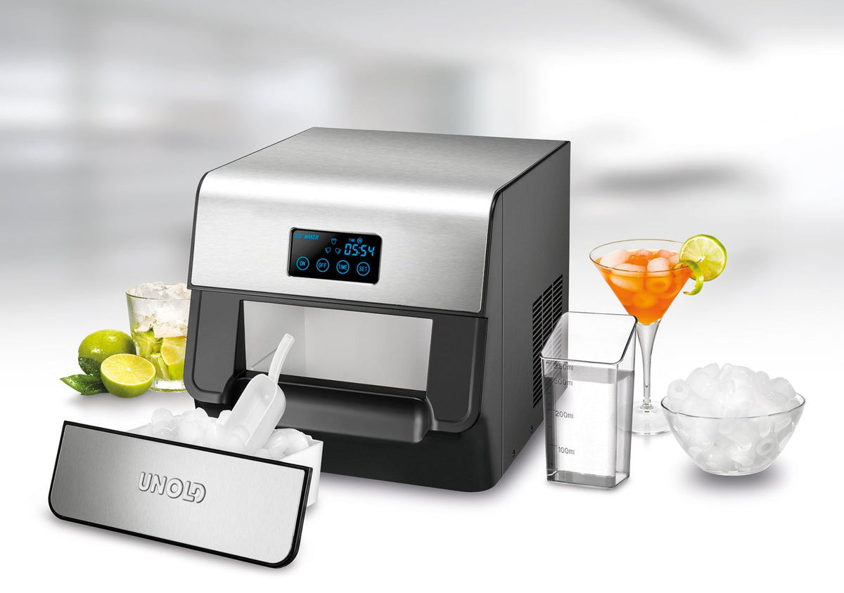 Eine Eismaschine mit Digitalanzeige ist abgebildet. Umgeben von einem Glas Eis, einem Cocktail, Limetten und einem Messbecher. Die Vorderseite der Eismaschine ist geöffnet und zeigt frisch zubereitete Eiswürfel.