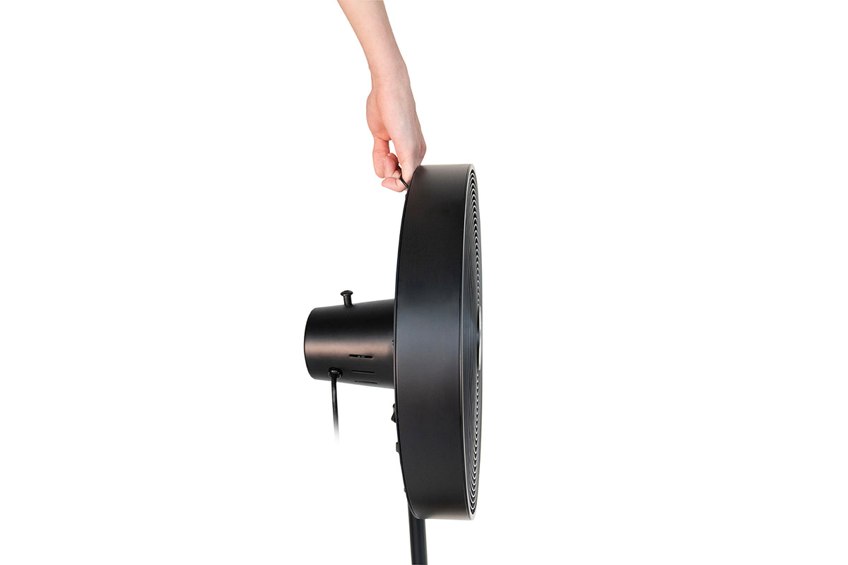 Eine Hand greift nach der Oberkante des Unold Standventilators Black Steel, einem schwarzen runden elektrischen Ventilator, der im Profil vor einem weißen Hintergrund zu sehen ist.