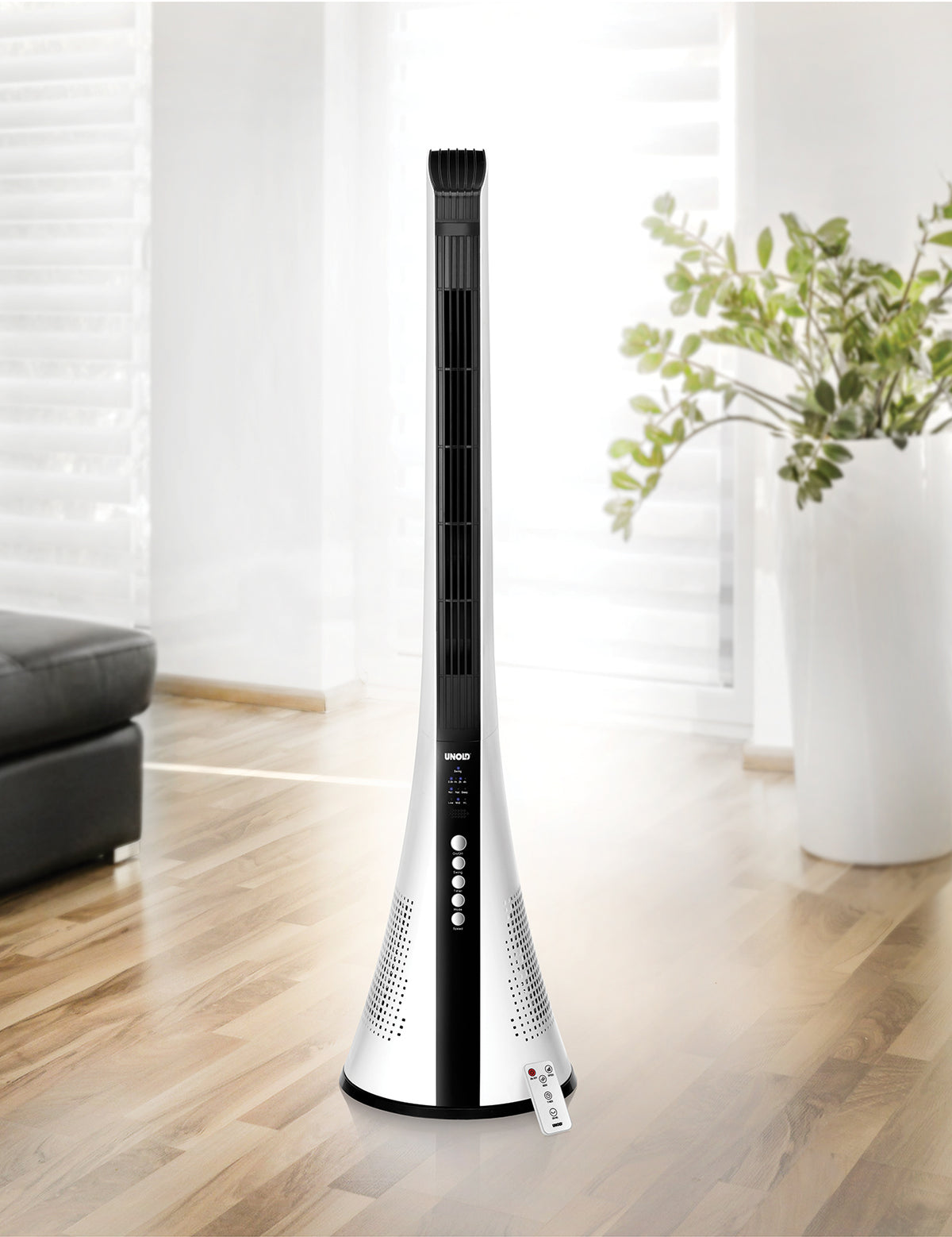 Der Unold TURMVENTILATOR VIEW, ein moderner schwarz-weißer Turmventilator mit Bedienknöpfen und Fernbedienung, steht auf einem Holzboden in einem hellen Wohnzimmer mit Sofa, großen Fenstern und einer Topfpflanze im Hintergrund.