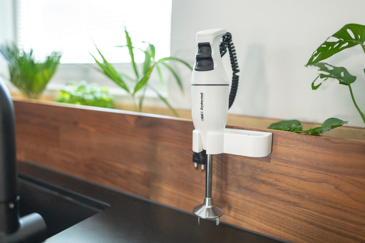 Der Stabmixer Unold ESGE-Zauberstab® E 120 Select Weiß ist auf einer Holzrückwand in einer modernen Küche montiert, im Hintergrund sind auf der Fensterbank grüne Pflanzen zu sehen.