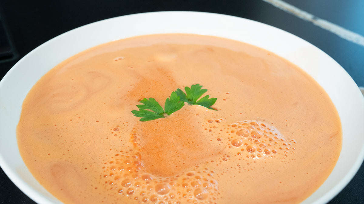 Eine Schüssel cremige Orangensuppe, garniert mit drei Zweigen frischer Petersilie in der Mitte. Die Suppe hat eine schaumige Konsistenz mit kleinen Bläschen an der Oberfläche.