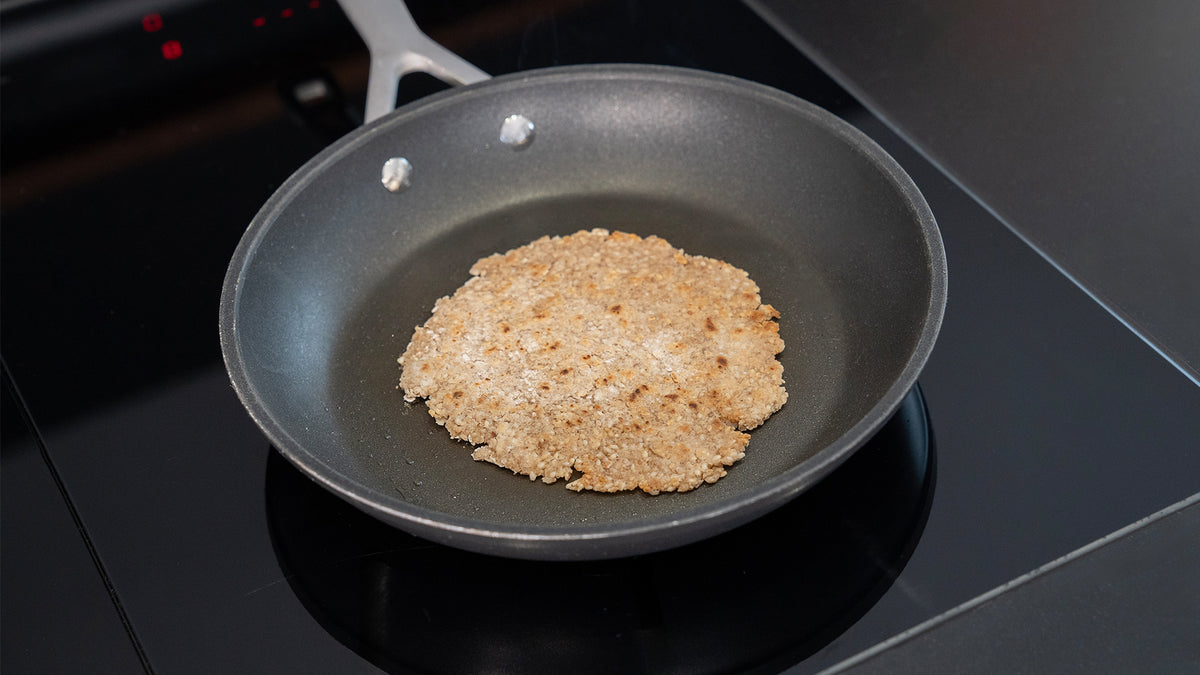 Eine runde, flache, goldbraune Tortilla oder ein Fladenbrot wird in einer schwarzen, antihaftbeschichteten Bratpfanne auf einer schwarzen Glaskochplatte gebacken.