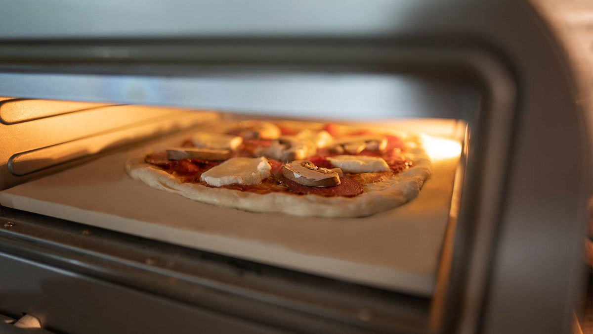Eine mit Käse und Pilzen belegte Pizza wird auf einem Stein in einem Pizzaofen gebacken, wobei der Rand zu backen beginnt und der Käse zu schmelzen beginnt.