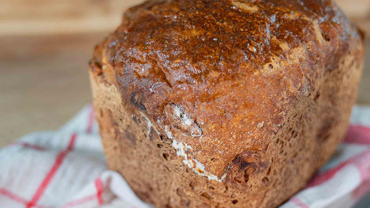 Eine Nahaufnahme eines frisch gebackenen Brotlaibs mit goldbrauner Kruste, der auf einem weiß-rot karierten Tuch liegt.