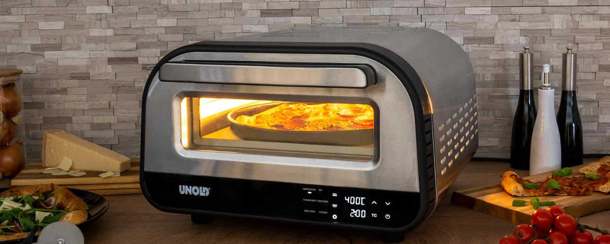Ein Pizzaofen für die Arbeitsplatte mit Digitalanzeige zeigt den Pizzabackvorgang im Inneren an. Der Ofen steht auf einer Küchentheke, in deren Nähe sich Zutaten wie Käse, Tomaten und Kräuter befinden.