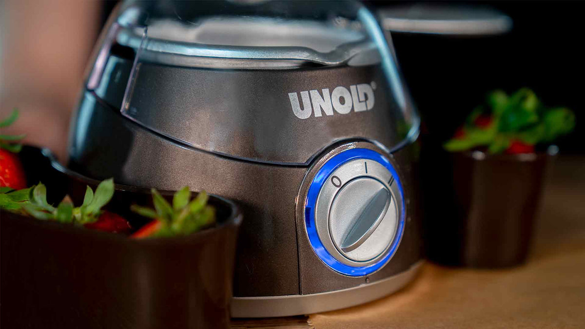 Eine Nahaufnahme eines UNOLD-Küchengeräts mit einem blau beleuchteten Drehregler, das auf einer Theke neben Schüsseln mit frischen Erdbeeren steht.