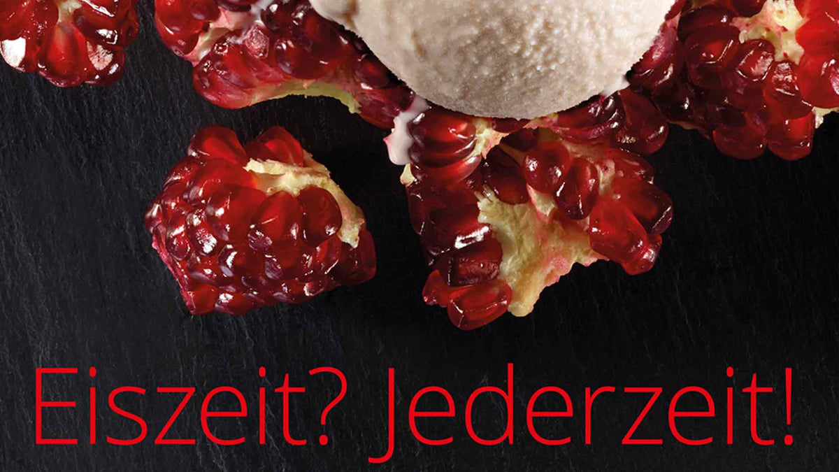 Eine Kugel Eis liegt auf Granatapfelkernen auf einer dunklen Oberfläche. Unten steht in kräftigem Rot: „Eiszeit? Jederzeit!“.