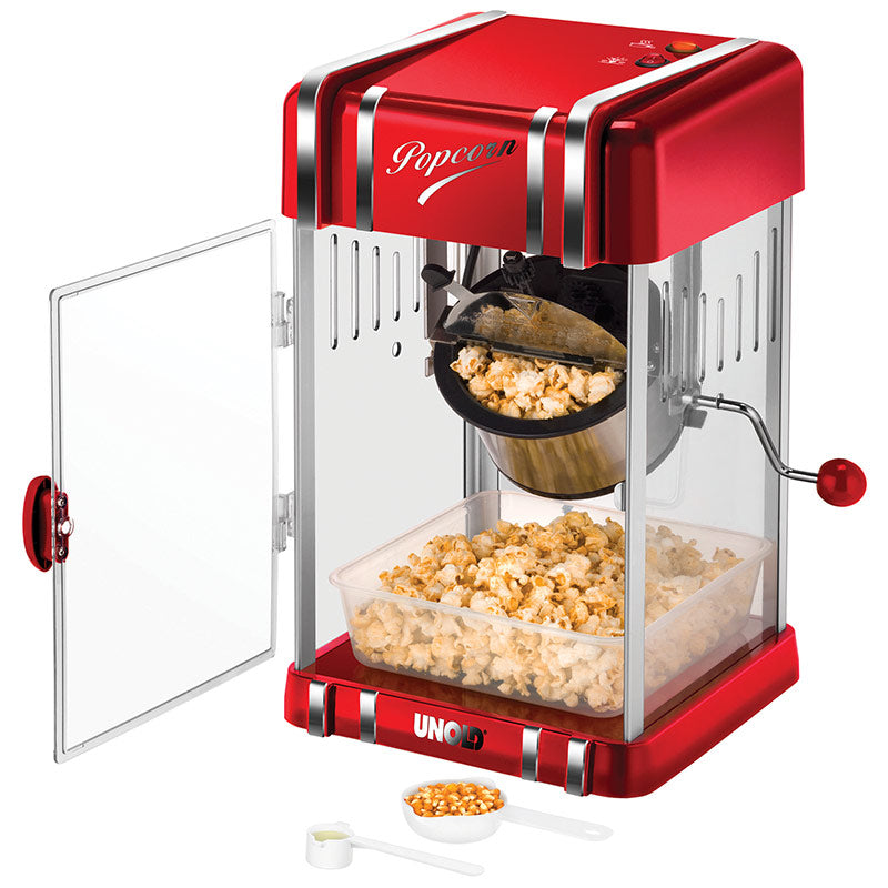 Der Unold Popcornmaker Retro verfügt über ein rot-silbernes Retro-Design mit einer transparenten Tür, einem sichtbaren Metallkessel, in dem Popcorn knallt, einer Schale zum Auffangen des Popcorns darunter und einer Schaufel mit Körnern vorne.